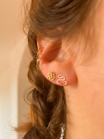 Oreille de femme avec une petite boucle d'oreille en forme de fleur dorée et une petite boucle d'oreille en forme de serpent doré