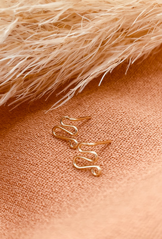 Petites boucles d'oreilles dorées en forme de serpent en fil gold filled sur fond de tissu orange