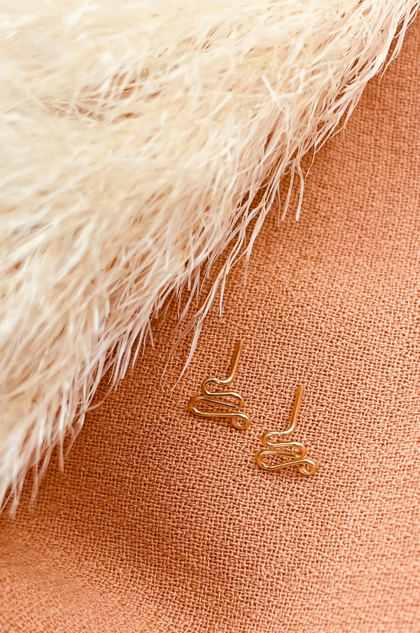 Petites boucles d'oreilles dorées en forme de serpent en fil gold filled sur fond de tissu orange